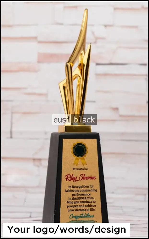 A custom-designed trophy with a polished gold abstract blade-like sculpture on a black rectangular base, featuring a gold plaque with a black seal and personalized text, set against a light brick wall background.