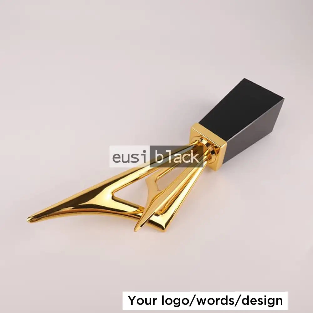A modern lipstick or cosmetic tube with a glossy gold geometric metal body and a matte black rectangular cap, photographed on a clean light gray background.